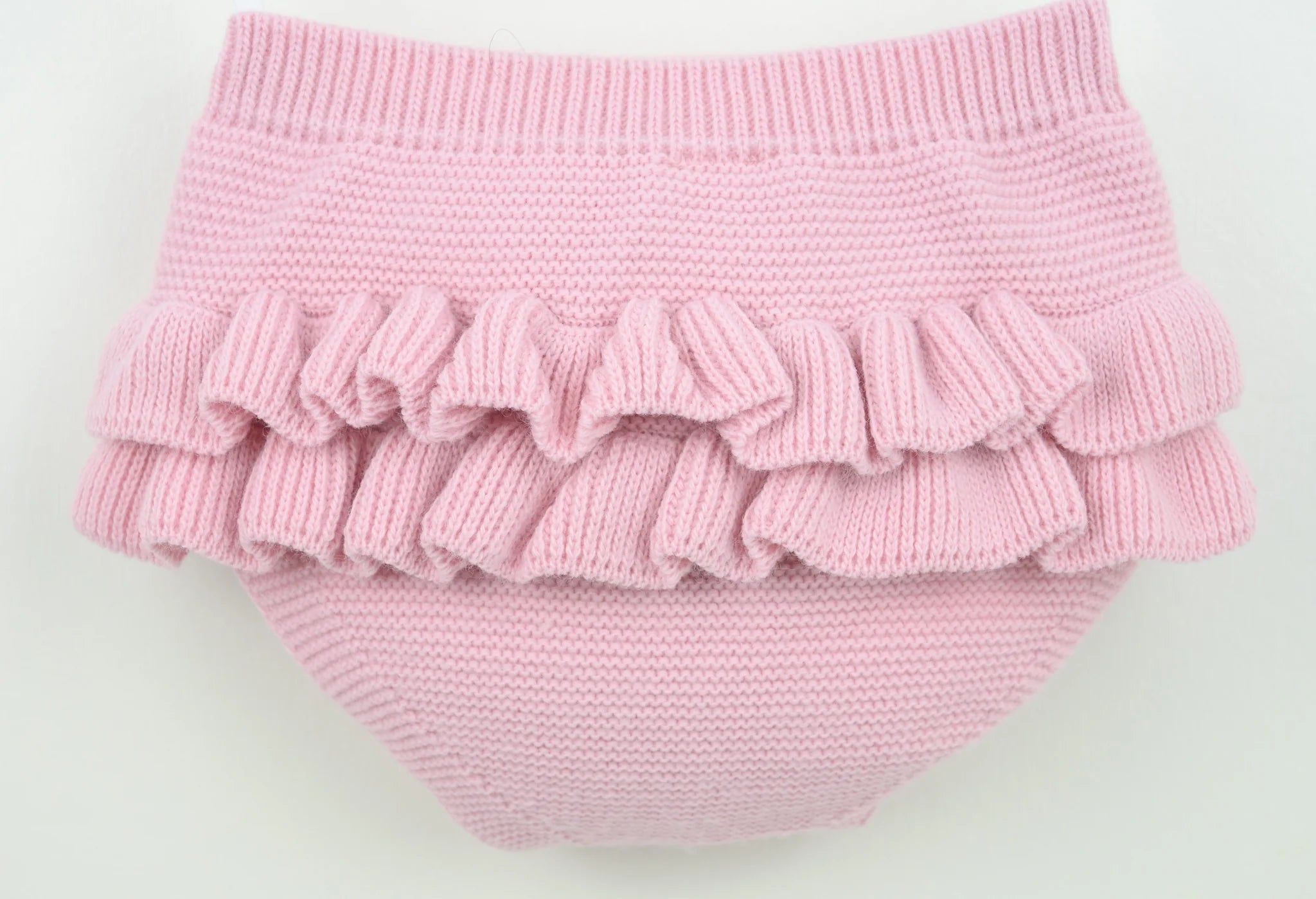 Pink knitted baby bloomers with ruffles on a light gray background